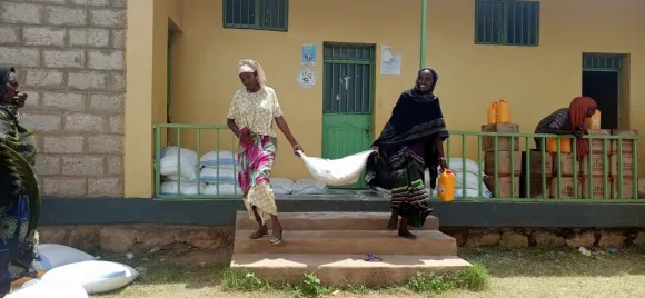 Zwei Frauen tragen einen Sack mit Lebensmitteln die Treppe herunter. 