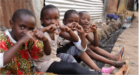 Mädchen aus dem Dorothea Rescue Center sitzen in einer Reihe und machen ein Herz mit ihren Händen. 