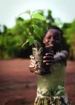 Mädchen in Afrika steht draußen und hält Pflanze in der Hand. 